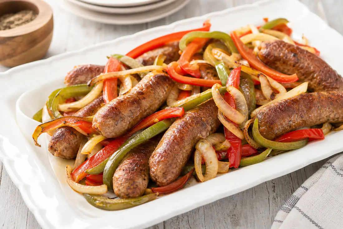 Browned Italian sausage links with red and green bell pepper strips and onions on a white platter
