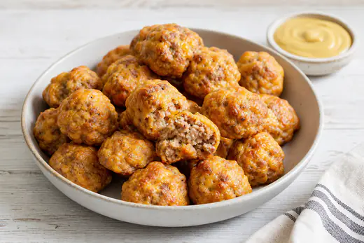 Golden brown cheesy sausage balls in a bowl with a small dish of honey mustard