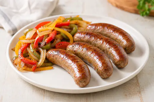 Browned Italian sausage links on a plate with sliced peppers and onions