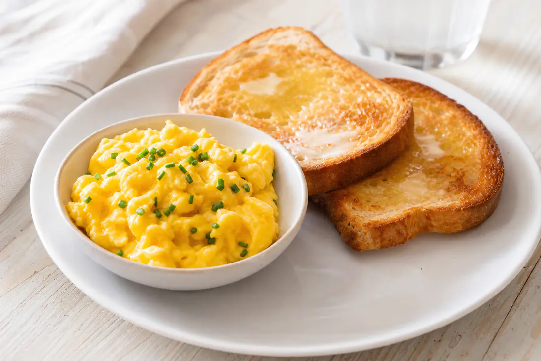 Soft fluffy scrambled eggs with chives in a small round pan next to buttered toast