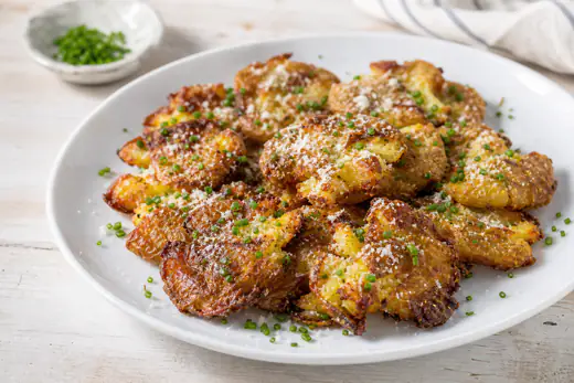 Crispy flattened smashed potatoes with Parmesan and chives on a plate
