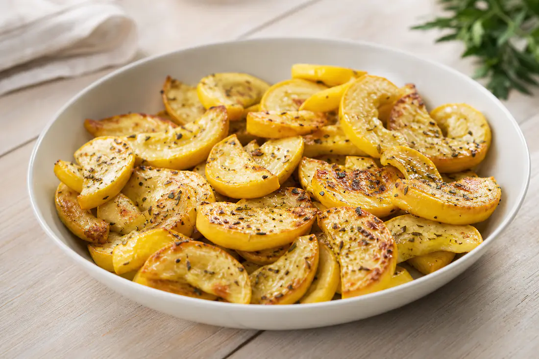 Golden roasted yellow squash half-moons with herbs in a white bowl
