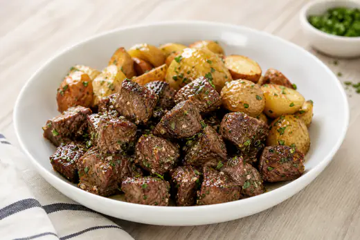 Browned sirloin steak bites tossed in garlic butter and parsley in a white bowl