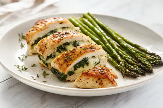 Sliced stuffed chicken breast showing a spinach and melted cheese filling on a plate with asparagus