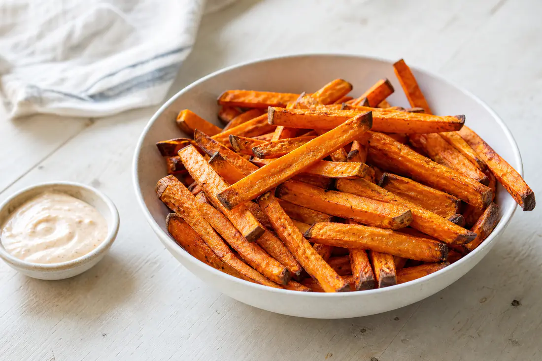 Golden crispy sweet potato fries in a bowl with a small dish of dipping sauce