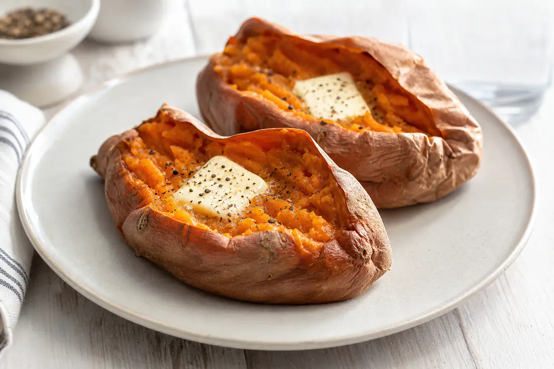 Whole baked sweet potatoes split open with orange flesh and a pat of butter