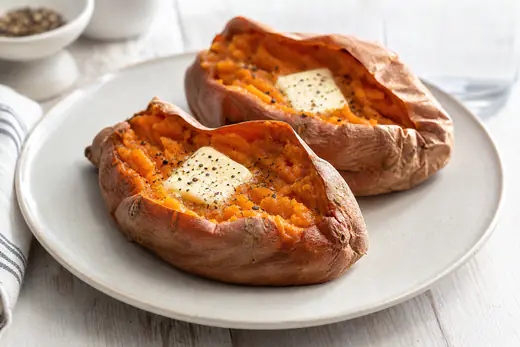 Whole baked sweet potatoes split open with orange flesh and a pat of butter