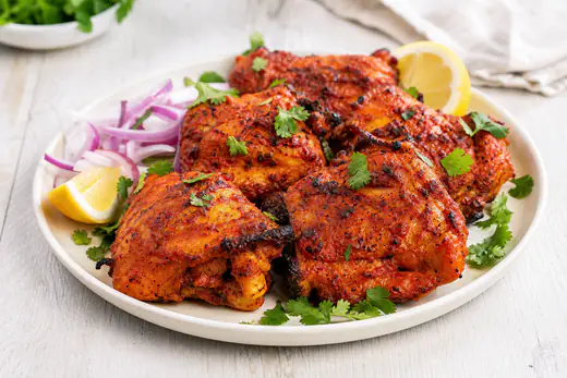 Red charred tandoori chicken thighs with lemon wedges and sliced red onion
