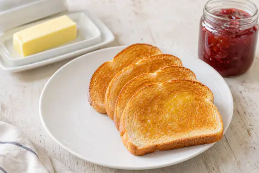 Four slices of golden buttered toast stacked on a white plate