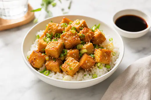 Golden crispy air fryer tofu cubes in a white bowl with sliced scallions and sesame seeds