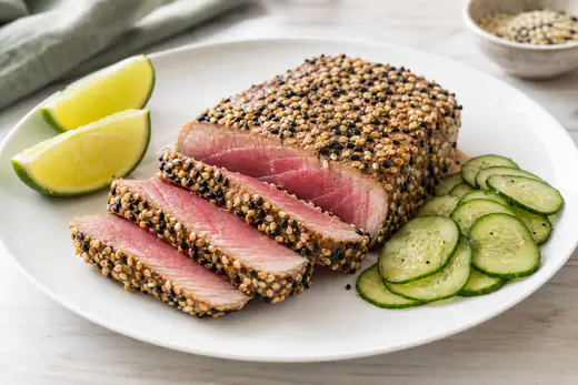 Sliced seared tuna steak with sesame seeds and lime wedges on a plate