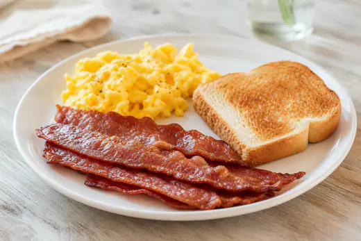Crispy slices of turkey bacon on a white plate with scrambled eggs and toast
