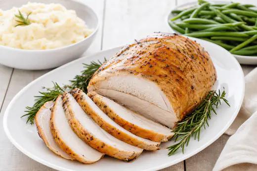 Sliced roast turkey breast with golden skin on a white platter with rosemary