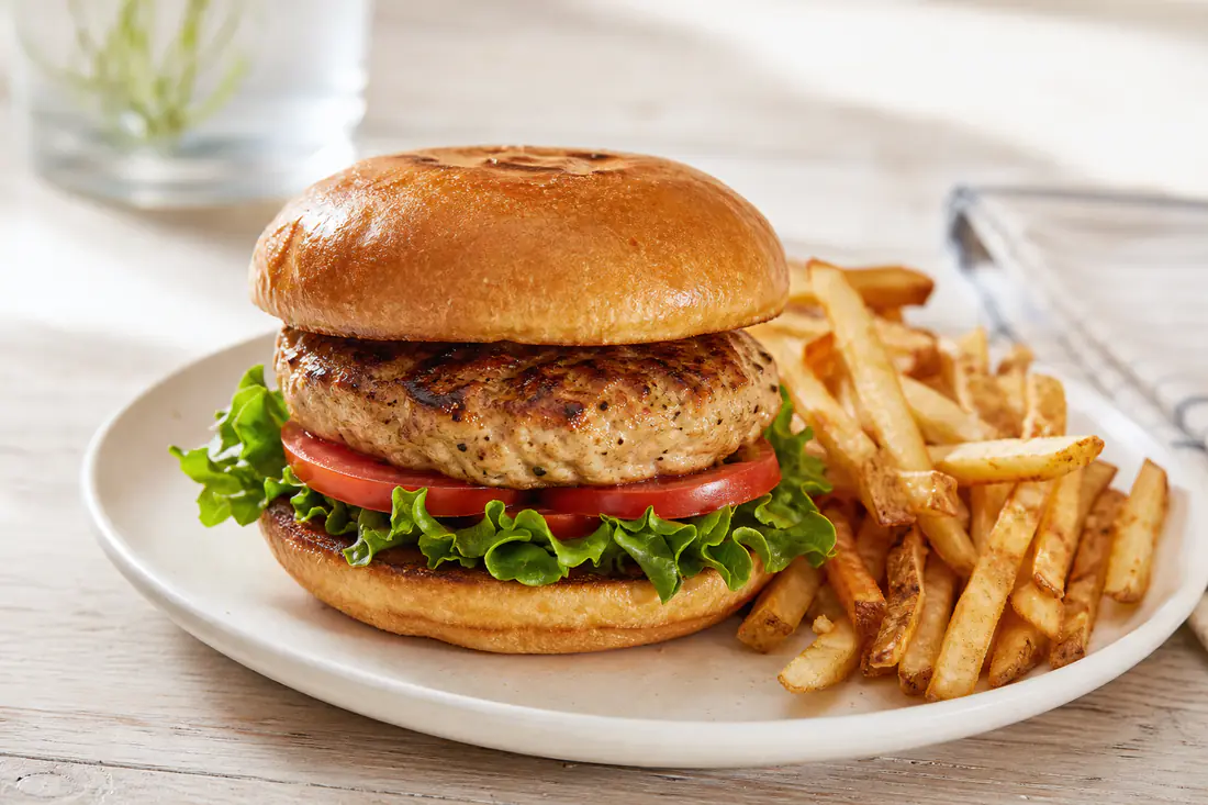 Turkey burger on a toasted bun with lettuce and tomato next to a pile of fries