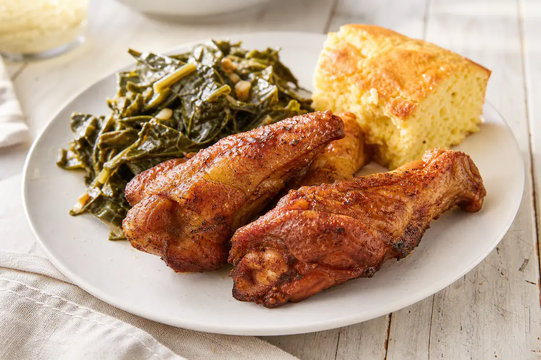 Crispy golden brown turkey wing sections on a plate with collard greens and cornbread