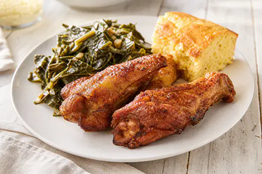 Crispy golden brown turkey wing sections on a plate with collard greens and cornbread