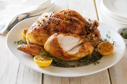 Whole roasted chicken with golden crispy skin on a platter with lemon and thyme